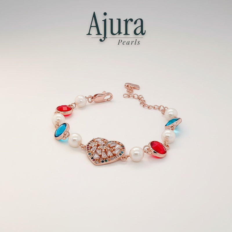 Ajura Pearls rose gold bracelet with freshwater pearls, red and blue gems, and a heart-shaped charm.