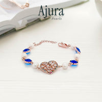 Ajura Pearls rose gold bracelet with freshwater pearls, blue gems, and a heart-shaped charm encrusted with colorful crystals.
