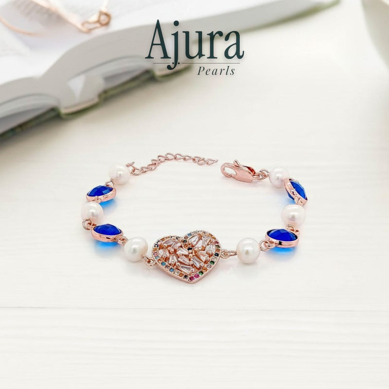 Ajura Pearls rose gold bracelet with freshwater pearls, blue gems, and a heart-shaped charm encrusted with colorful crystals.